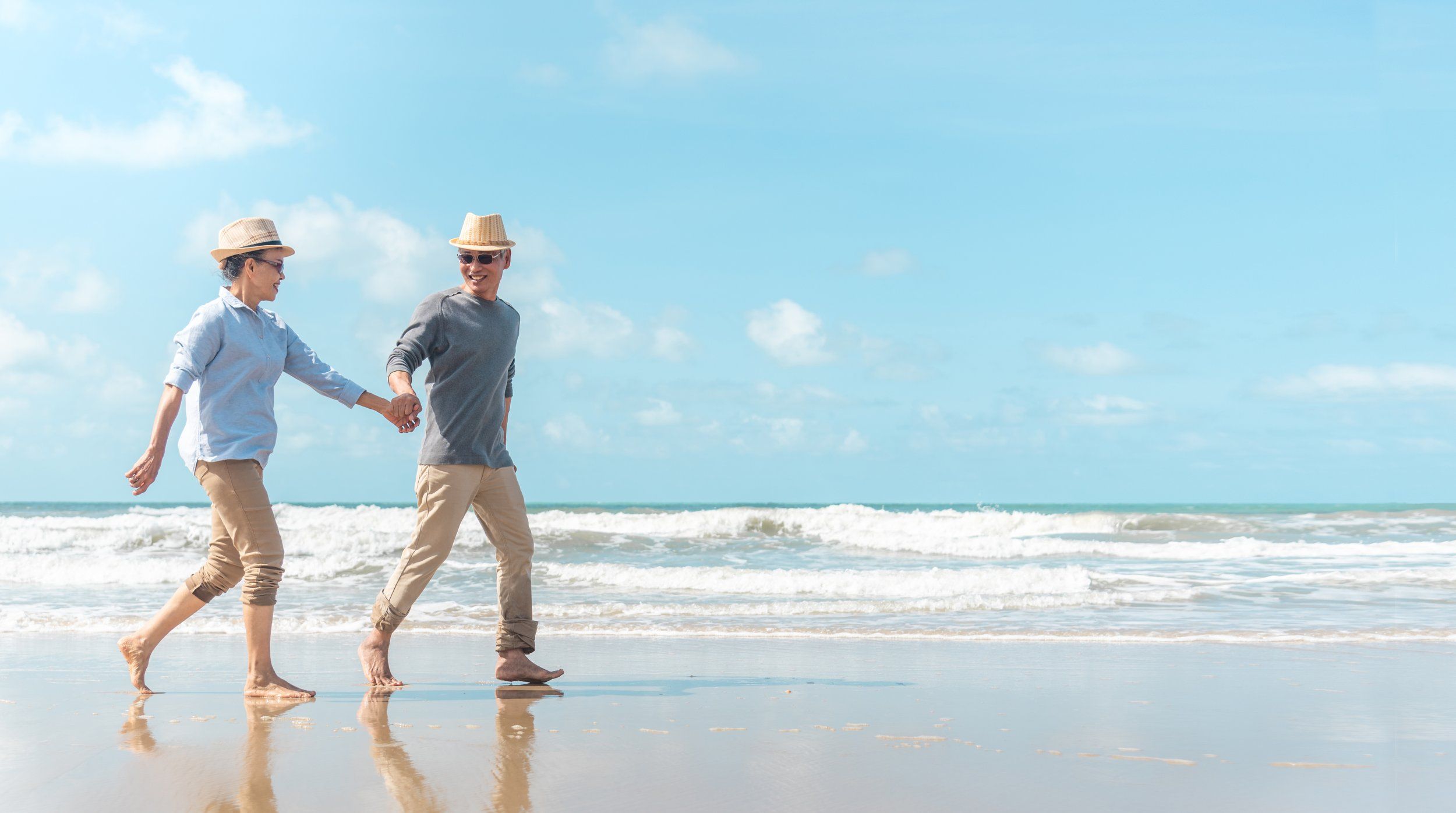 An older couple walking hand in hand along a sunny beach